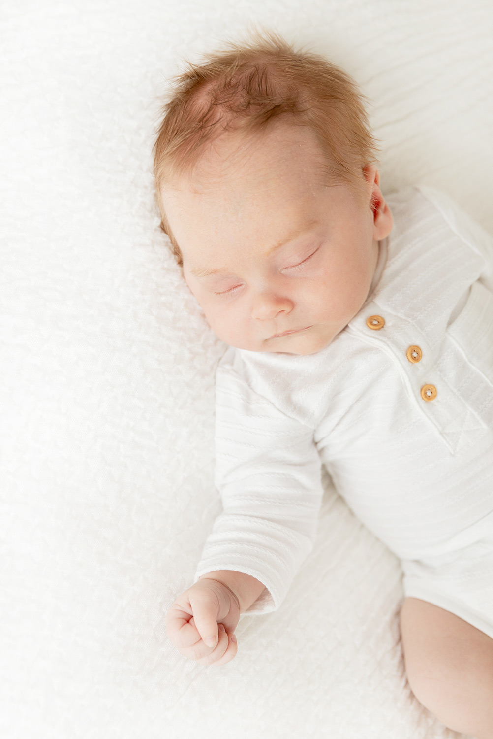Baby in weißem Body liegt auf weißer Decke