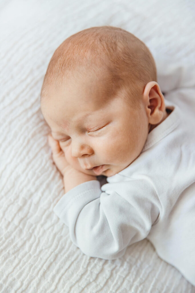 Neugeborenes Baby in einer weißem Body, fotografiert in natürlichem Licht für natürliche Neugeborenenfotografie in Fürstenfeldbruck und Puchheim.