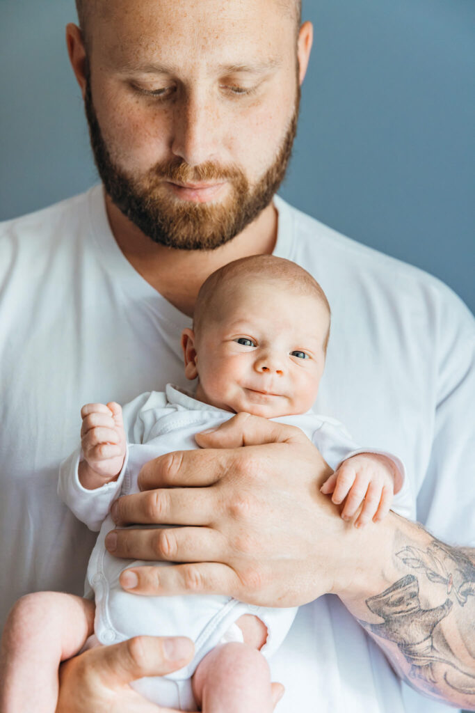 Neugeborenes Baby in Papa Armen, fotografiert in natürlichem Licht für natürliche Neugeborenenfotografie in Fürstenfeldbruck und Puchheim.
